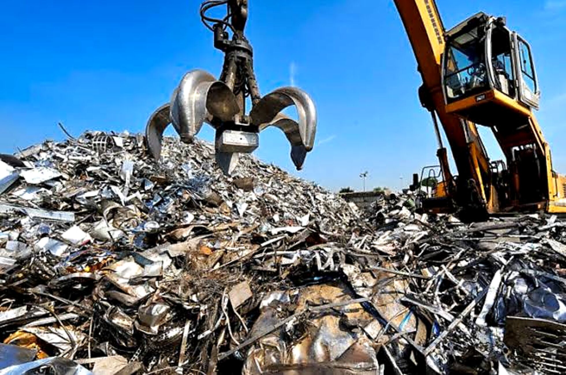 Excavator with grapple attachment processing scrap metal pile